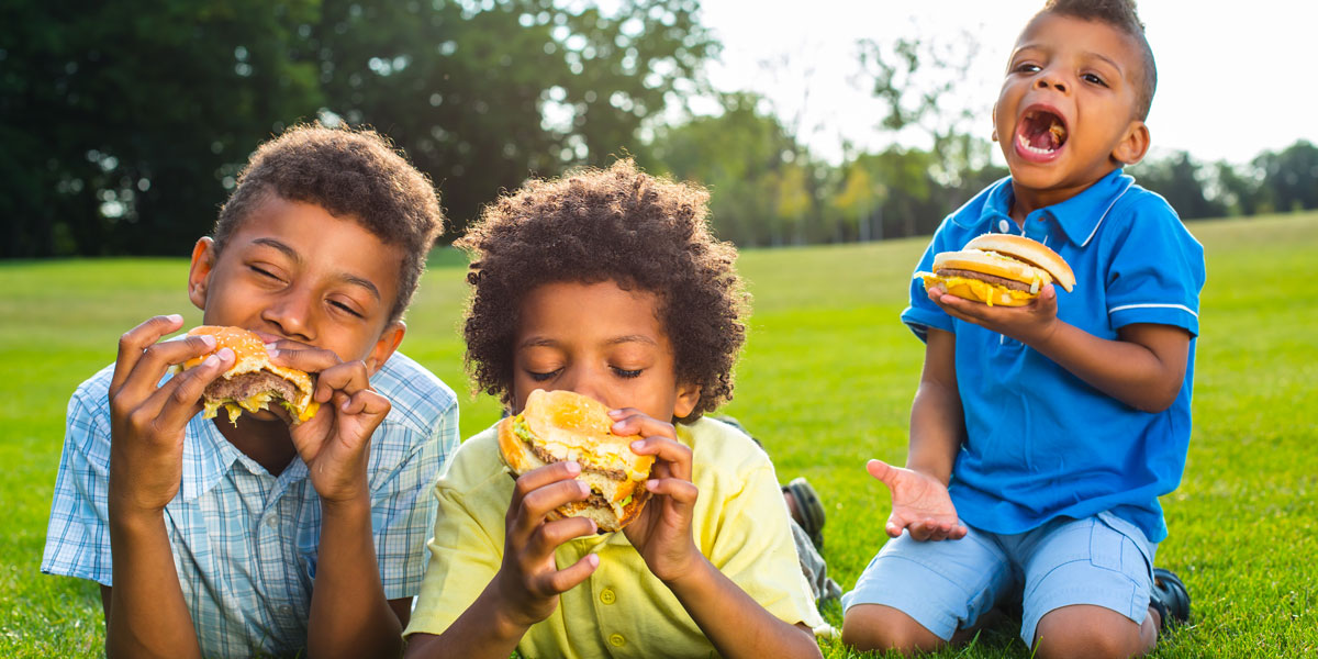 Three kids eating beef burgers